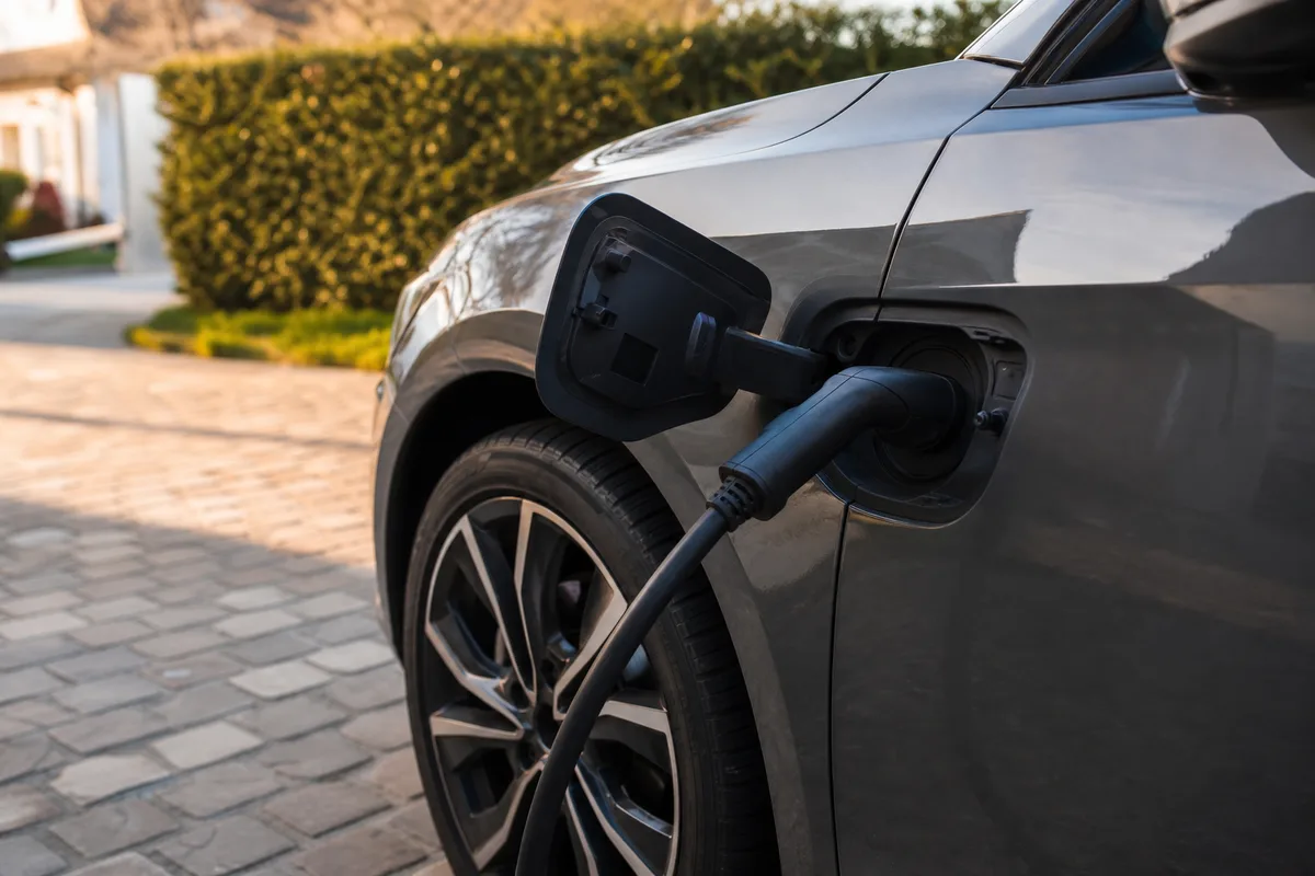 Prise de recharge domestique branchée sur le côté avant d&rsquo;une berline compacte dans une allée pavillonnaire