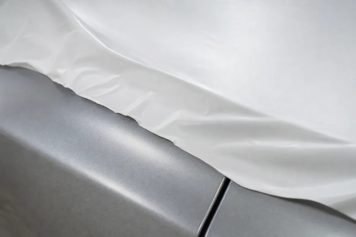 Film de protection blanc sur le capot d’une voiture neuve, gros plan sur la carrosserie