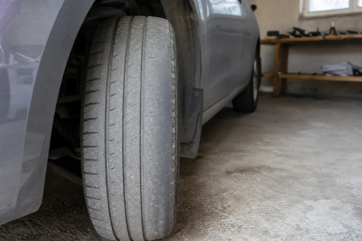 Roue avant braquée d’une voiture montrant l’usure asymétrique d’un pneu dans un garage